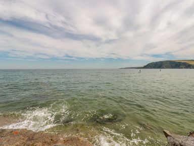 An ocean view with gentle waves and two paddle boarders near a rocky coastline at Josie in Pentewan