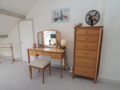 A dressing table with a mirror and stool next to a chest of drawers with a fan on top in a room at Eider Cottage in Warkworth