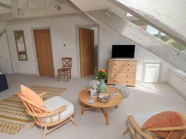 A living room with wooden chairs a round wooden coffee table a chest of drawers and a television at Eider Cottage in Warkworth