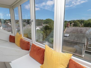 A window seat with orange and yellow cushions overlooking rooftops and trees at Eider Cottage in Warkworth