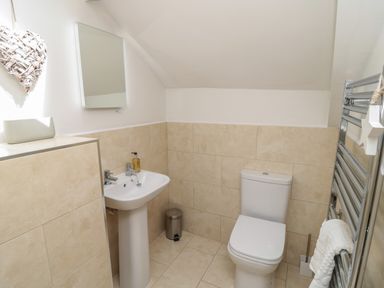 A bathroom with a pedestal sink, toilet, mirror, towel rack, and beige tiled walls at Eider Cottage in Warkworth