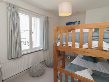 A bedroom with wooden bunk beds striped curtains and knitted poufs at Eider Cottage in Warkworth