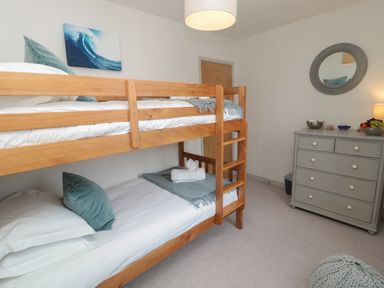 A bedroom with wooden bunk beds a gray dresser with a round mirror and a hanging light at Eider Cottage in Warkworth