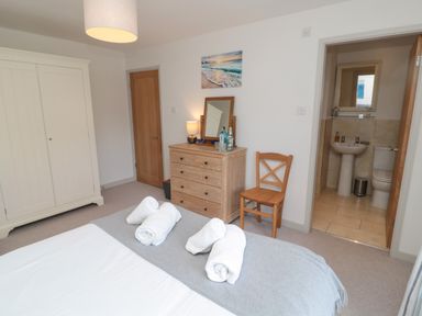 A bedroom with a bed, wooden dresser, chair, wardrobe, and an open door leading to a bathroom at Eider Cottage in Warkworth