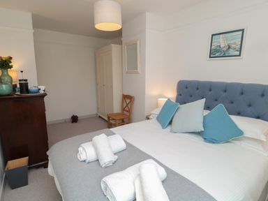 A bedroom with a bed with blue headboard and pillows wardrobe chair and chest of drawers at Eider Cottage in Warkworth