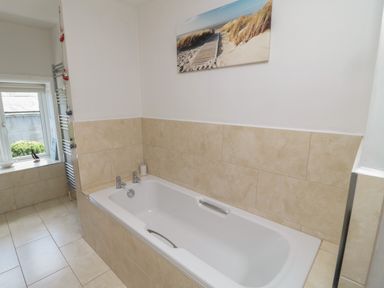 A bathroom with a bathtub tiled with beige tiles and a window with a heating rack at Eider Cottage in Warkworth