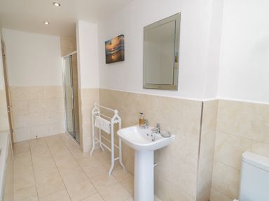A bathroom with a pedestal sink mirror towel rack shower and toilet at Eider Cottage in Warkworth