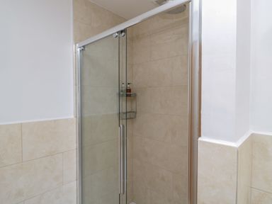 A shower with glass doors and beige tiled walls at Eider Cottage in Warkworth