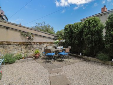 An outdoor patio area with a round table and four chairs on stone tiles surrounded by gravel and greenery