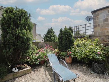 An outdoor garden area with a lounge chair surrounded by flowering plants and shrubs at Eider Cottage in Warkworth