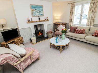 A living room with a fireplace a sofa armchairs a round coffee table and a television at Eider Cottage in Warkworth