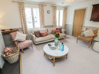 A sitting room with a sofa armchairs a round coffee table and windows with curtains at Eider Cottage in Warkworth