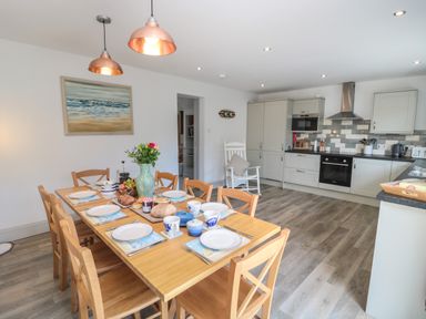 A kitchen and dining area with a wooden table set for breakfast and grey cabinets at Eider Cottage in Warkworth