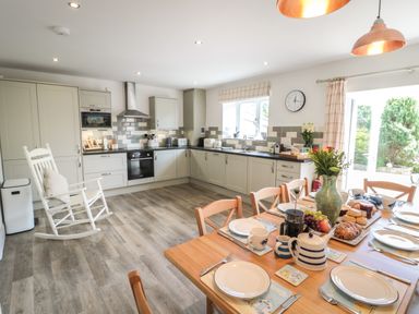 A kitchen with light grey cabinets a dining table set with plates and a vase of flowers at Eider Cottage in Warkworth