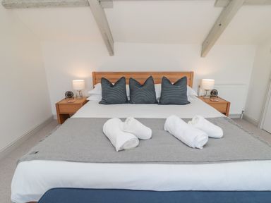 A bedroom with a bed with three pillows and rolled towels on a blanket at Eider Cottage in Warkworth