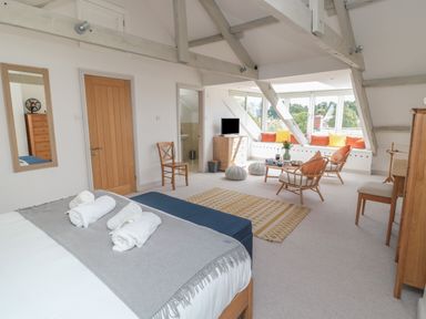 A bedroom with a bed, chairs, a rug, window seating with cushions, and wooden furniture at Eider Cottage in Warkworth