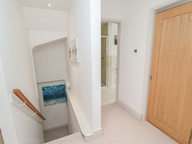 A hallway with stairs, a wooden door, and a view into a bathroom at Eider Cottage in Warkworth