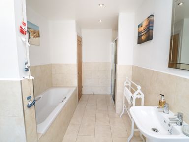 A bathroom with a bathtub on the left side a shower enclosure straight ahead a white sink with faucets on the right side and beach-themed decorations on the walls at Eider Cottage in Warkworth