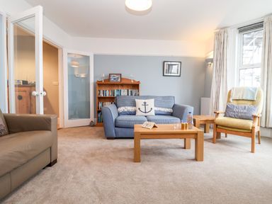 A living room with sofas a wooden coffee table bookshelf and large windows at 11 The Craighurst in Southwold