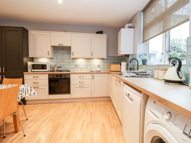 A kitchen with white cabinets wooden countertops a microwave stove sink washing machine and dining table at 11 The Craighurst in Southwold