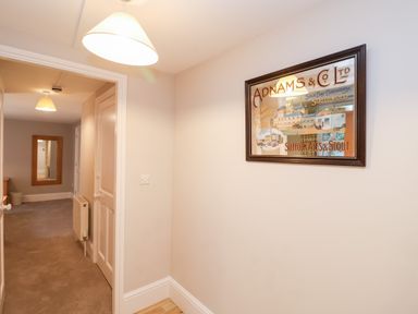 A hallway with a framed sign on the wall two hanging ceiling lights a radiator a door and a mirror at 11 The Craighurst in Southwold