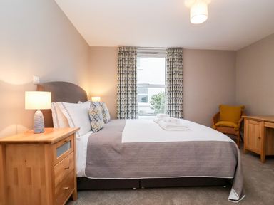 A bedroom with a double bed bedside tables lamps patterned curtains a chair and a desk at 11 The Craighurst Southwold
