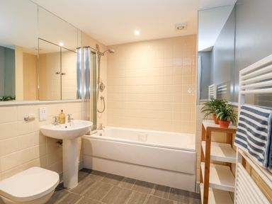 A bathroom with a bathtub shower sink toilet towel rail and shelf with plants at 11 The Craighurst in Southwold