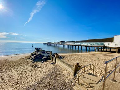 A sandy beach with a wooden groyne and rocks leading to a pier extending over calm sea water at 11 The Craighurst in Southwold