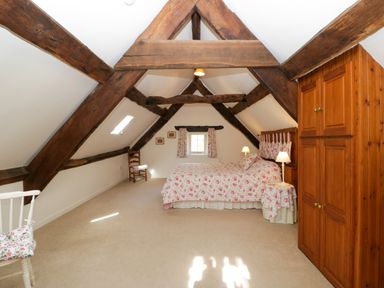 A bedroom with exposed wooden beams a bed with floral bedding wooden wardrobe and chairs at Anvil Cottage in Gatcombe near Blakeney