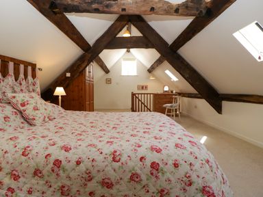 A bedroom with floral bedspread and exposed wooden beams at Anvil Cottage Gatcombe near Blakeney