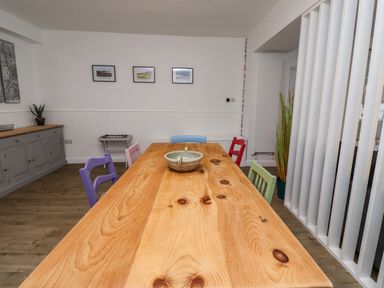 A dining room with a wooden table surrounded by colorful chairs and wall art at 2A Front Street in Embleton