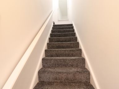 A carpeted staircase with white walls and a handrail leading to a mirror at 2A Front Street in Embleton