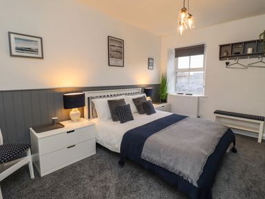 A bedroom with a double bed two bedside tables two lamps a window and wall shelves at 2A Front Street in Embleton