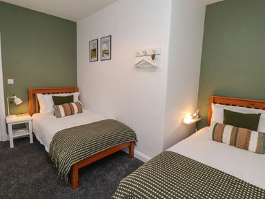 A bedroom with two single beds green accent walls and bedside tables with lamps at 2A Front Street Embleton