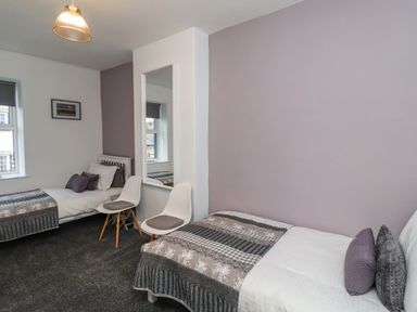 A bedroom with two single beds two white chairs a mirror and a window at 2A Front Street in Embleton