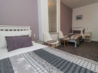 A bedroom with two single beds white chairs a wall mirror and a side table at 2A Front Street in Embleton