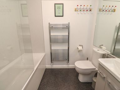A bathroom with a bathtub, a towel rack, a toilet, a sink with cabinets, and a wall hook at 2A Front Street Embleton