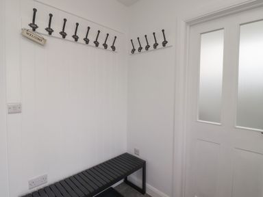 A corner of a room with multiple coat hooks a black bench and a white door at 2A Front Street in Embleton