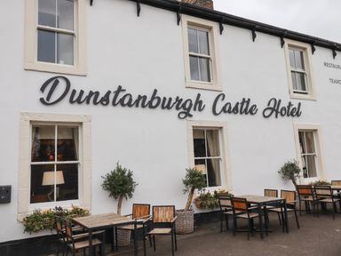 Outdoor seating area with tables, chairs, and potted plants outside Dunstanburgh Castle Hotel in Embleton