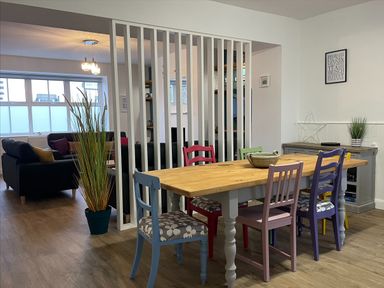 A dining area with a wooden table and colorful chairs next to a living space with sofas at 2A Front Street in Embleton