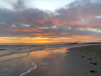 A beach with waves and a sunset reflecting on the water at 2A Front Street in Embleton
