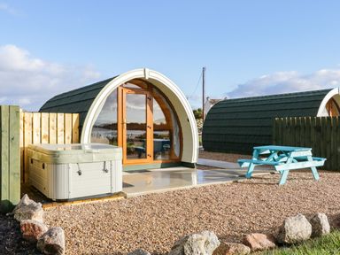 A curved wooden pod with glass doors a hot tub and a blue picnic table outside at The Wheelhouse Pod No 1 in Burtonport County Donegal