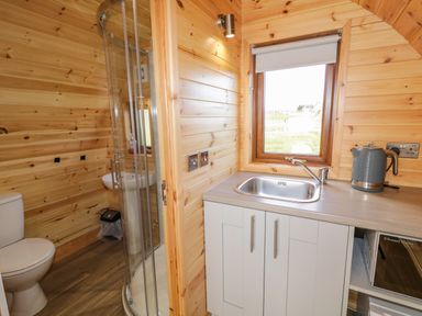 A kitchen sink area with a kettle and a microwave next to a bathroom with a shower and toilet at The Wheelhouse Pod No 1 Burtonport County Donegal