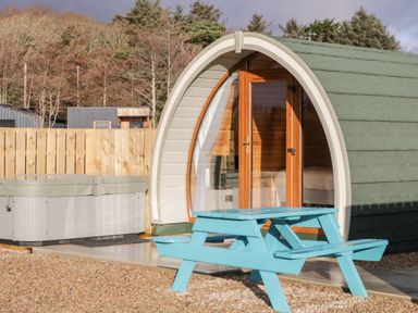 An outdoor scene with a small cabin pod with wooden doors a hot tub and a blue picnic table at The Wheelhouse Pod No 1 Burtonport County Donegal