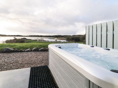 An outdoor hot tub with bubbling water next to a gravel path and grassy area by a lake at The Wheelhouse Pod No 1 Burtonport County Donegal