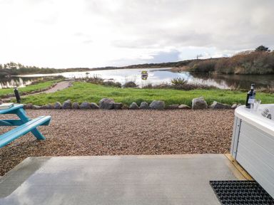 A lakeside view with a gravel path and picnic bench next to a hot tub with a bottle and glasses at The Wheelhouse Pod No 1 in Burtonport County Donegal
