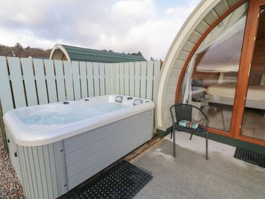 An outdoor area with a hot tub next to a chair and glass door leading to a bedroom at The Wheelhouse Pod No 1 in Burtonport County Donegal