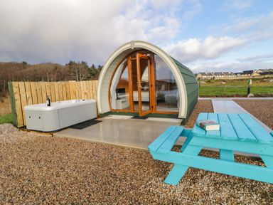 A small pod cabin with glass doors next to a hot tub and blue picnic table at The Wheelhouse Pod No 1 in Burtonport County Donegal