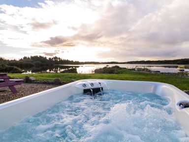 An outdoor hot tub with water jets near a grassy area and a body of water at The Wheelhouse Pod No 2 in Burtonport County Donegal