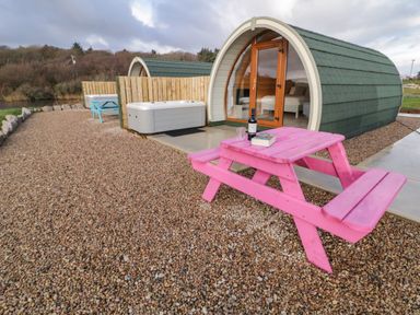 Small curved cabin with glass door next to a pink picnic table and hot tub on a gravel area at The Wheelhouse Pod No 2 in Burtonport County Donegal